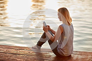 Female with cellphone sitting on riverÃ¢â¬â¢s dock